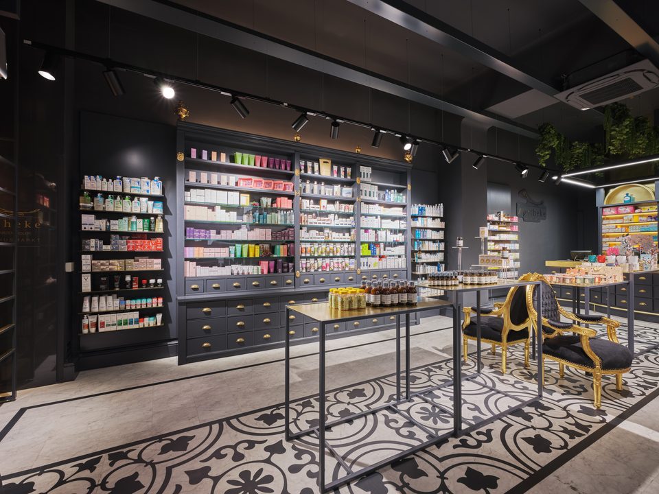 Verkaufsfläche der Apotheke Schwarzer Adler in Wien mit zwei Mitteltischen und vergoldeten Barockstühlen über dem schwarz-weißen Ornamentboden