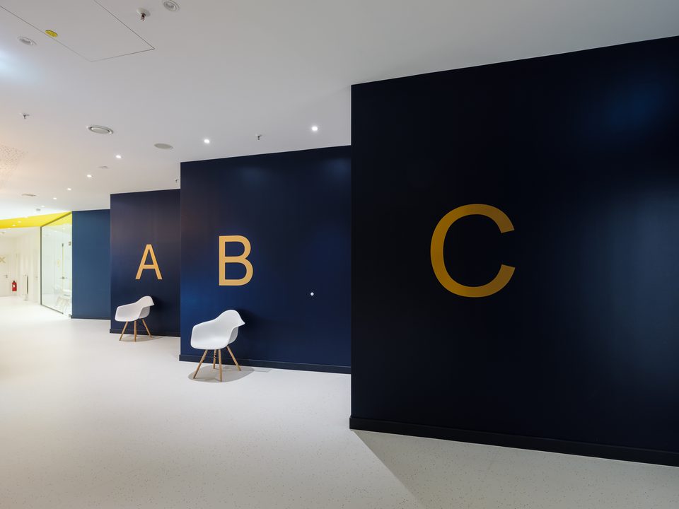 Wartezonen der Augenarztpraxis im DEZ, gegliedert durch dunkelblaue Wandscheiben mit den goldenen Buchstaben A, B und C