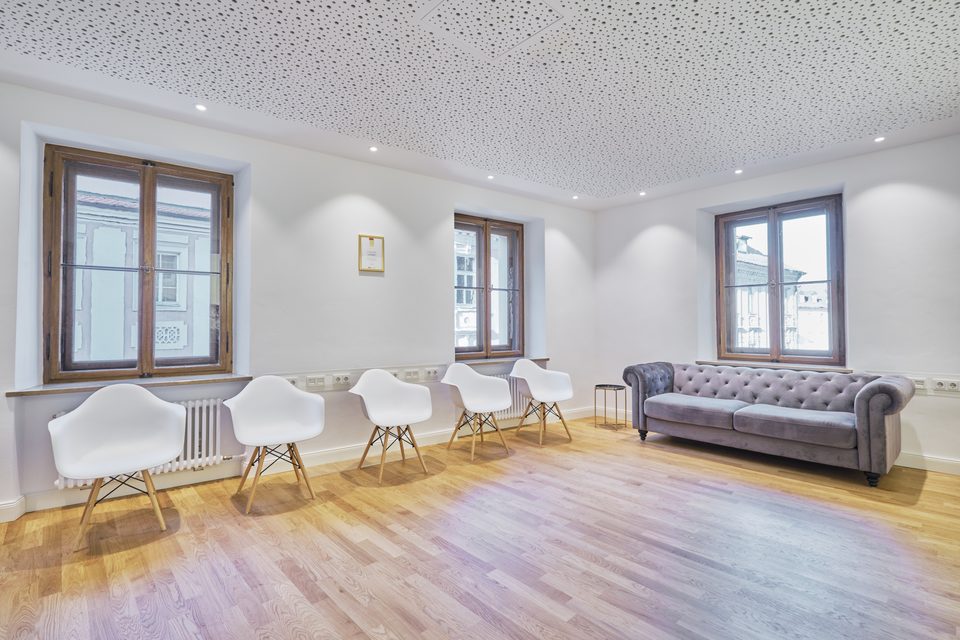 Wartezimmer im Altbau: Stuckdecke, Sprossenfenster, weiße Schalenstühle und ein lederner Chesterfield