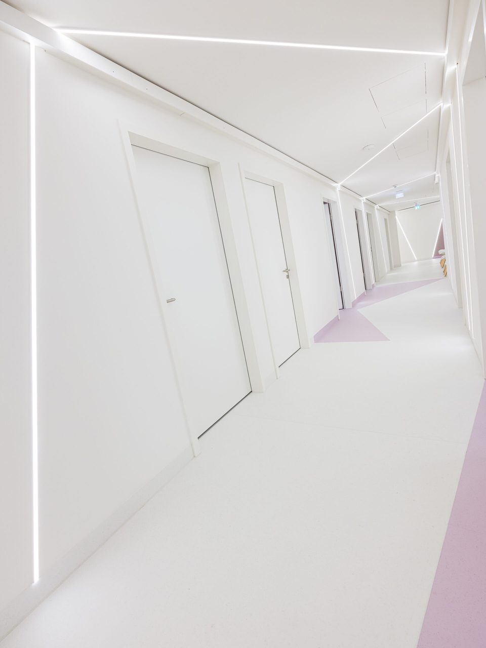Langer weißer Praxisflur mit Türen, den die durchlaufende LED-Linie in der Fluchtlinie begleitet
