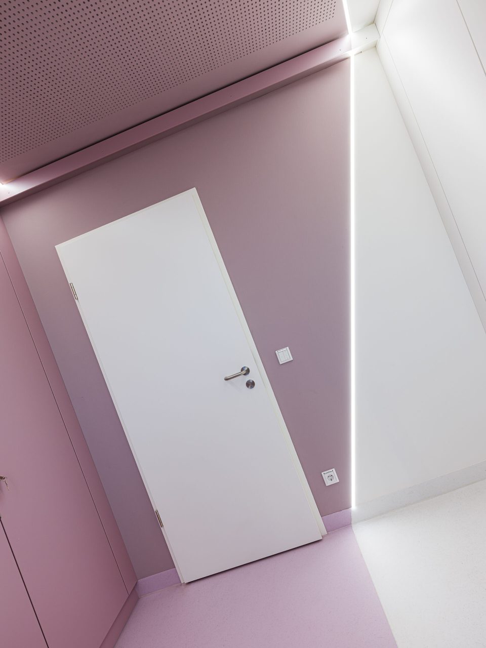 Weiße Tür in der roséfarbenen Wand, gerahmt von zwei Lichtlinien unter der perforierten Decke
