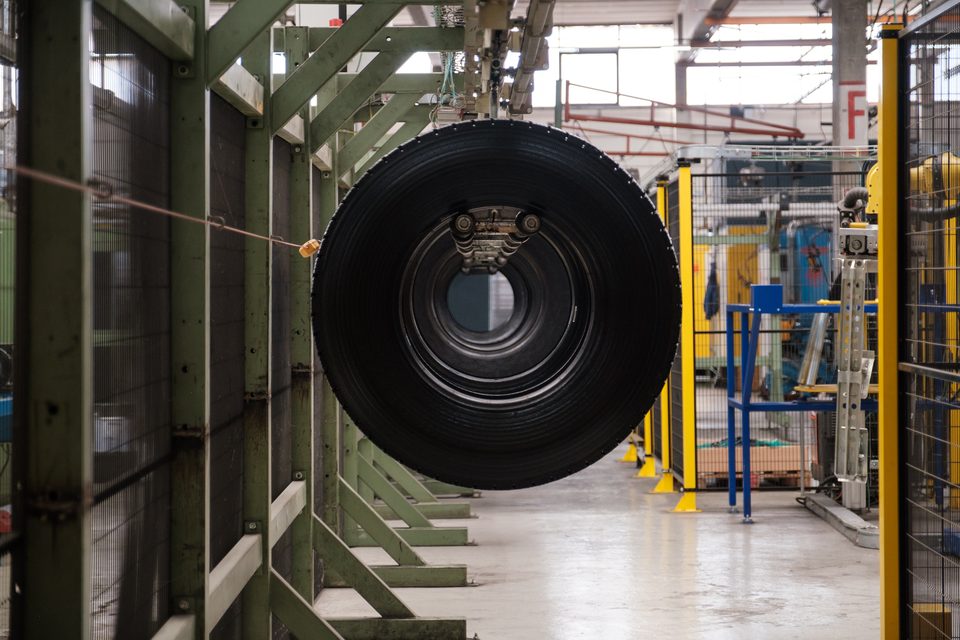 Ein LKW-Reifen hängt frei an der Fördertechnik in der Werkshalle, dahinter die Reihen der Bearbeitungsstationen