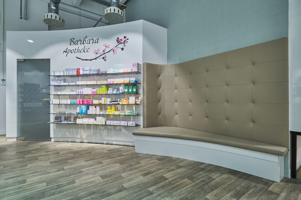 Ruhebereich der Barbara-Apotheke mit gepolsterter Sitzbank und Eingang zur Beratung