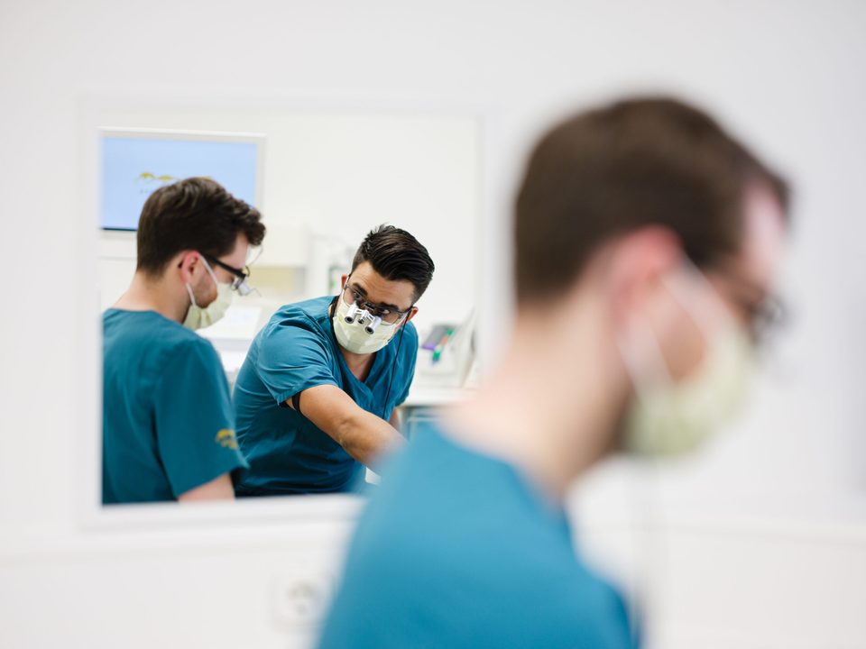 Zahnarzt und Assistenz bei der Behandlung, gespiegelt im Wandspiegel des Behandlungszimmers