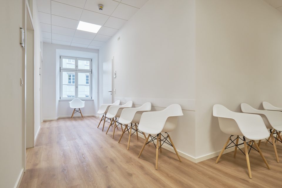 Heller Wartebereich mit Schalenstühlen entlang der Wand und Tageslicht aus dem Altbaufenster