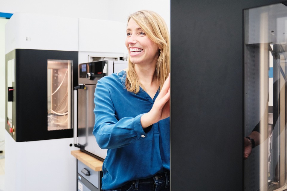 Die Gründerin von Kumovis lehnt lachend an ihrem 3D-Drucker für medizinische Bauteile