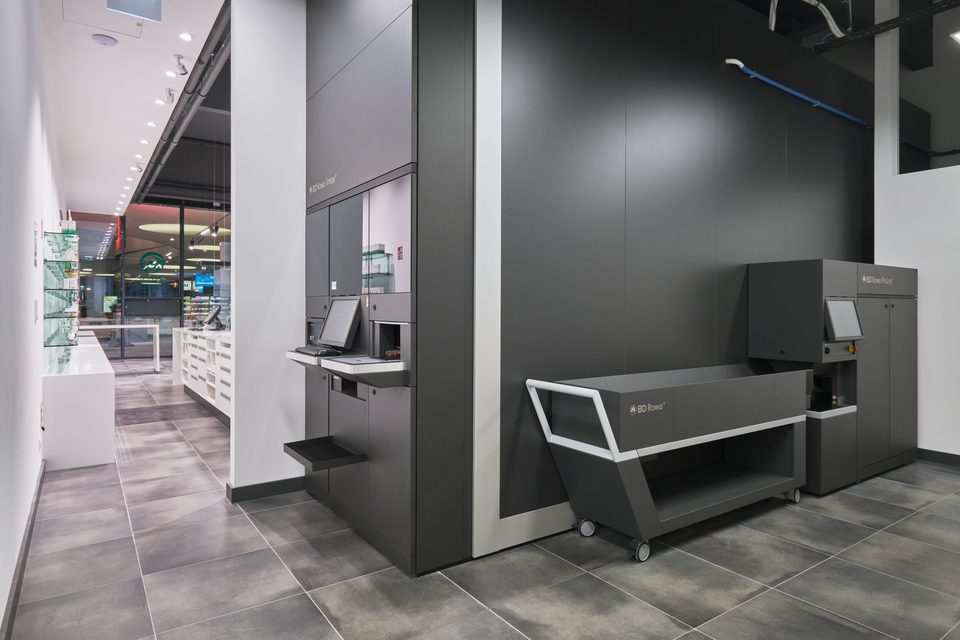 Blick von der dunklen Technikzone auf den Kommissionierautomaten, dahinter die helle Verkaufsfläche