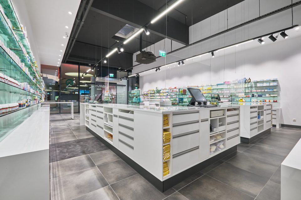 Offizin der Löwen-Apotheke mit weißen Einbaumöbeln vor dunkler Technikdecke, der Hochglanzboden spiegelt den Raum