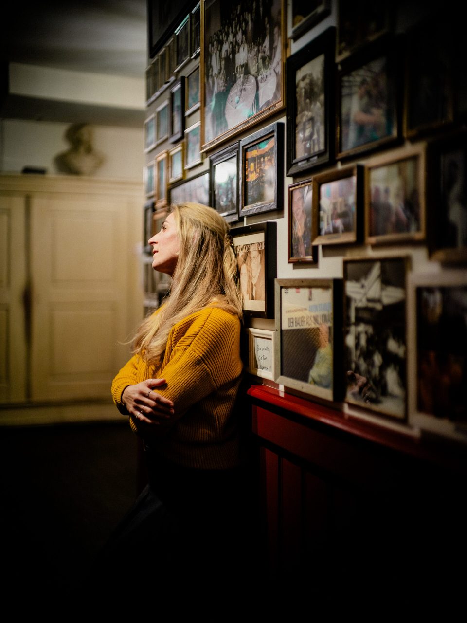 Frau lehnt seitlich vor einer Galerie aus eingerahmten Fotografien im Orphée