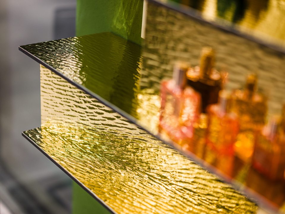 Nahaufnahme eines goldfarben hinterleuchteten Regalbodens, in dem sich Flakons und Verpackungen spiegeln