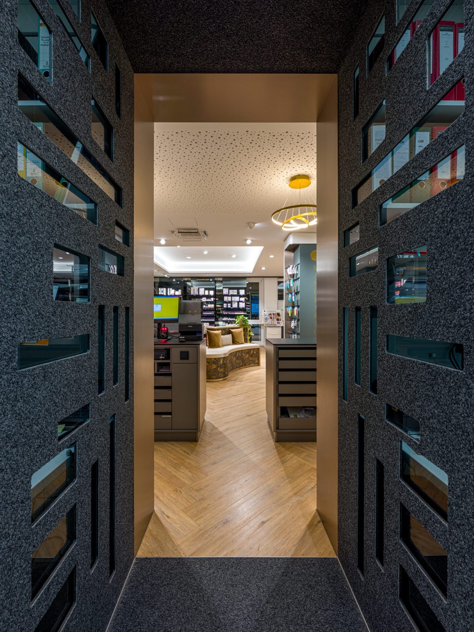 Durchgang mit dunklen Filzwänden und Blick in die Offizin der Rosenapotheke