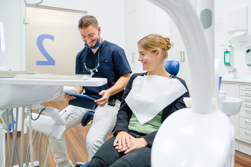 Zahnarzt im Gespräch mit einer Patientin am Behandlungsstuhl, beide lachen