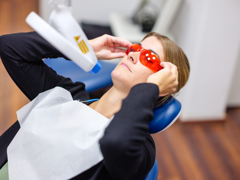 Patientin mit roter Schutzbrille, während die Behandlerin die Polymerisationslampe ansetzt